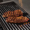 Two seasoned steaks are grilling on a hot grill.