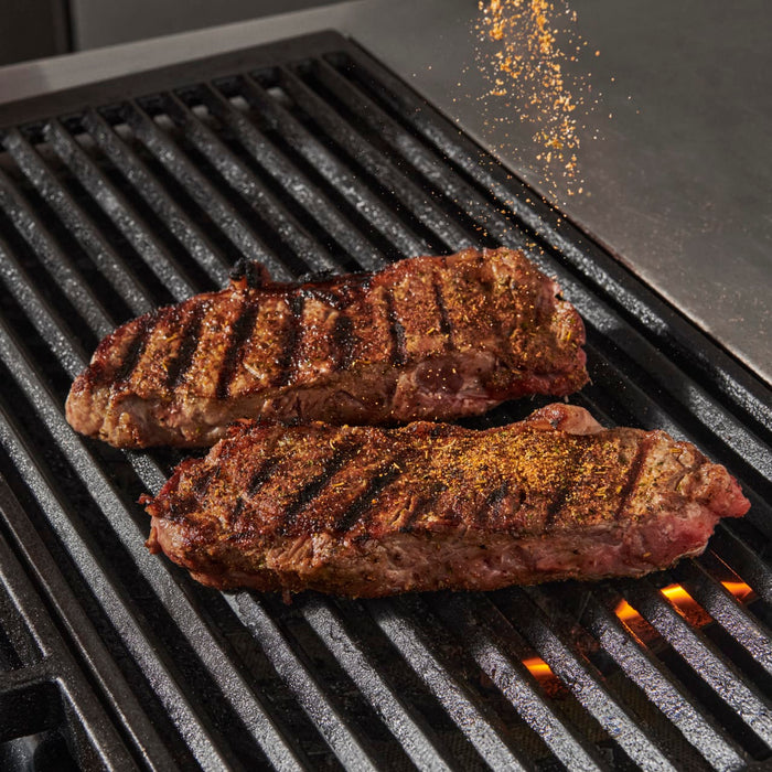 Two seasoned steaks are grilling on a hot grill.