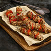 Three skewers of grilled chicken and red bell pepper are displayed on parchment paper atop a wooden board, suggesting a delicious and healthy meal option.