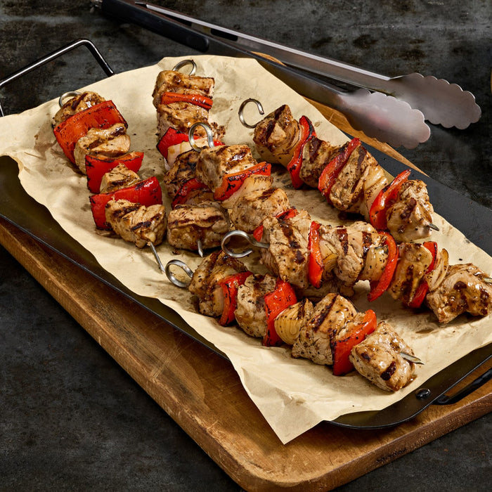 Three skewers of grilled chicken and red bell pepper are displayed on parchment paper atop a wooden board, suggesting a delicious and healthy meal option.