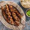 A platter of grilled meat skewers, prepared using Mccormick Grill Mates Asian Bbq Meat Marinade Mix 1.25 Oz, is served with a side of rice and chopped green onions.