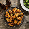 A top-down view of grilled chicken wings made with Mccormick Grill Mates Asian Bbq Meat Marinade Mix 1.25 Oz, served on a rustic wooden table with beer and green beans.