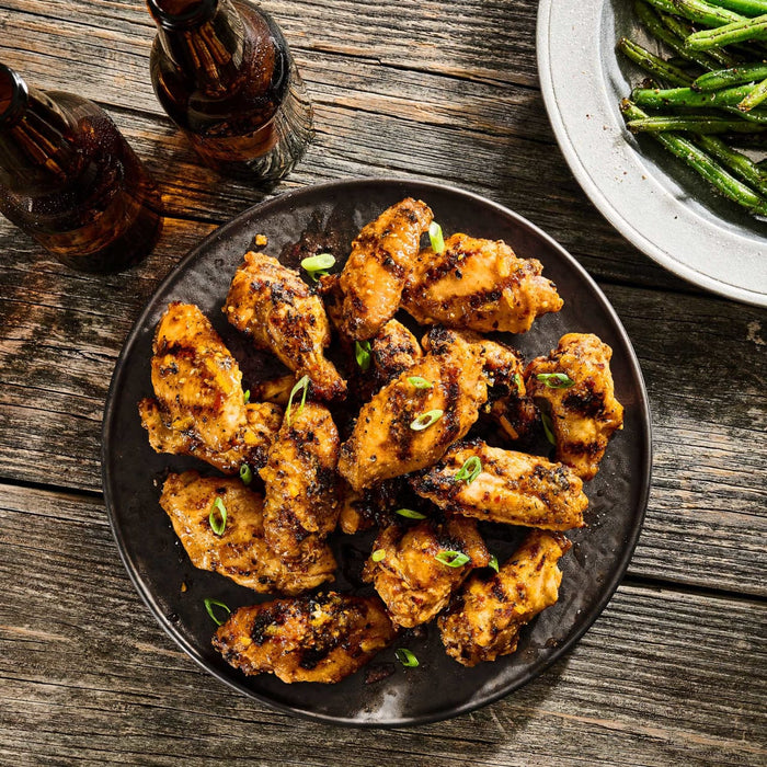 A top-down view of grilled chicken wings made with Mccormick Grill Mates Asian Bbq Meat Marinade Mix 1.25 Oz, served on a rustic wooden table with beer and green beans.