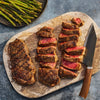A perfectly grilled steak, seasoned with Mccormick Grill Mates Signature Blend Seasoning, 6.53 Oz, is sliced on a wooden board next to a side of roasted asparagus.