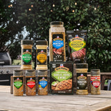 Collection of Grill Mates seasoning packets and jars on a wooden table with a grill in the background.
