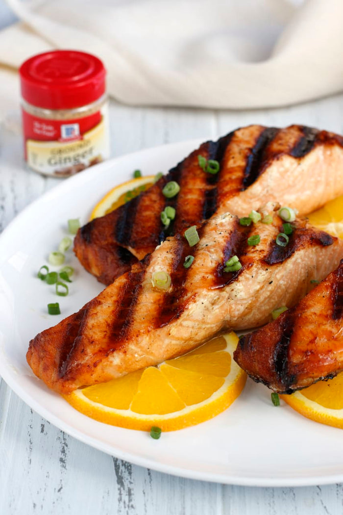 Grilled salmon fillets with orange slices and green onions on a white plate.