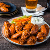 A platter of buffalo chicken wings coated in a rich orange sauce is served with celery sticks, carrot sticks, and a side of blue cheese dressing.