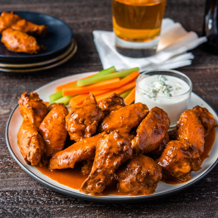 A platter of buffalo chicken wings coated in a rich orange sauce is served with celery sticks, carrot sticks, and a side of blue cheese dressing.