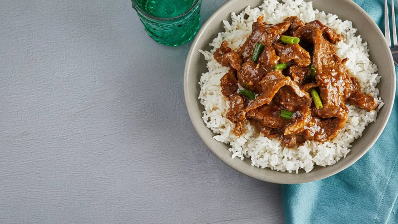 Bowl of rice with meat dish on a gray surface with a blue glass and napkin.