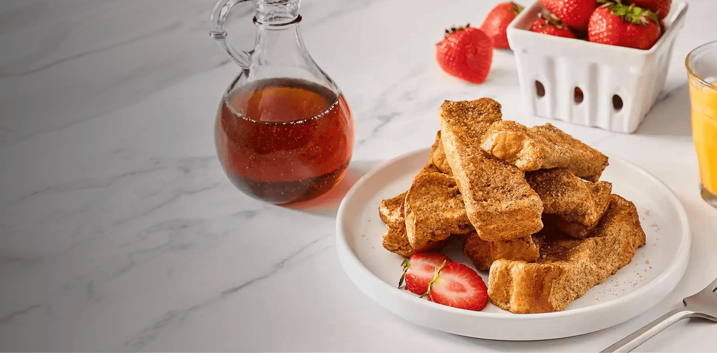 Stack of French toast on a plate with strawberries and syrup on a marble surface