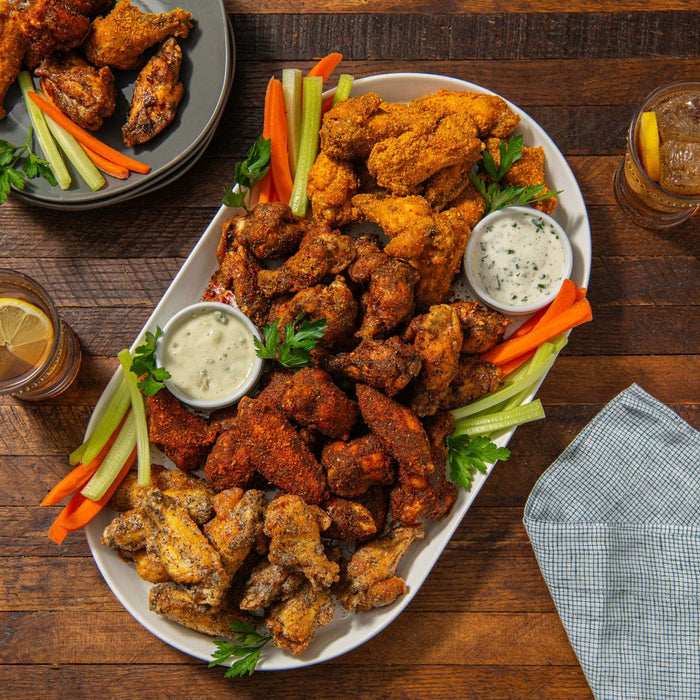 Platter of fried chicken with vegetables and dipping sauces on a wooden table.