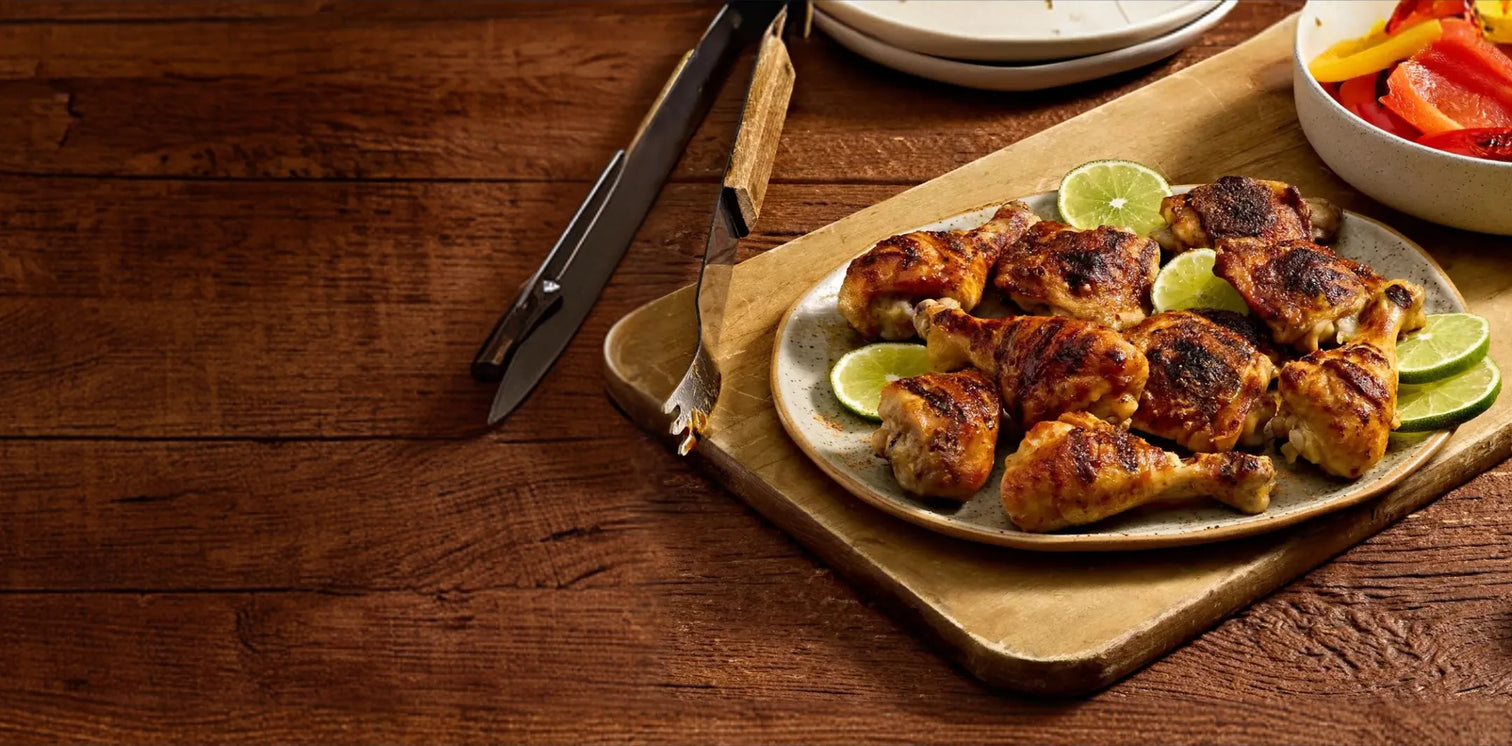 Plated chicken drumsticks with lime wedges on a wooden table