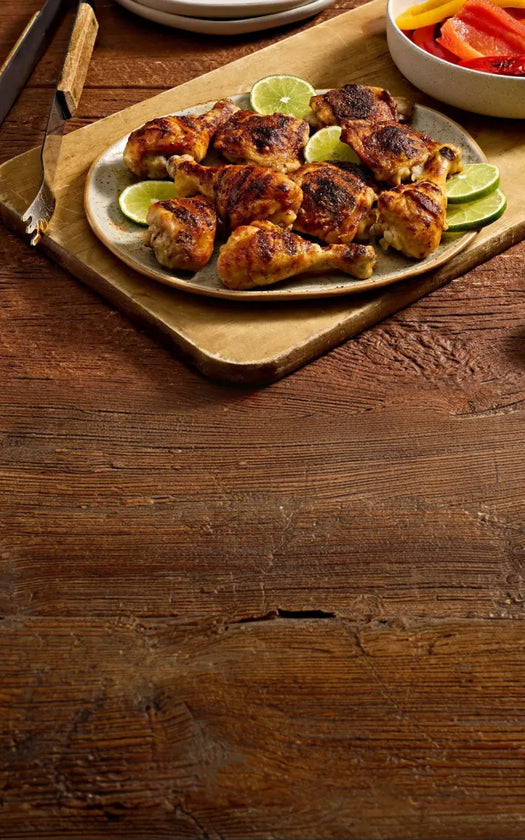 Plated chicken drumsticks with lime wedges on a wooden surface