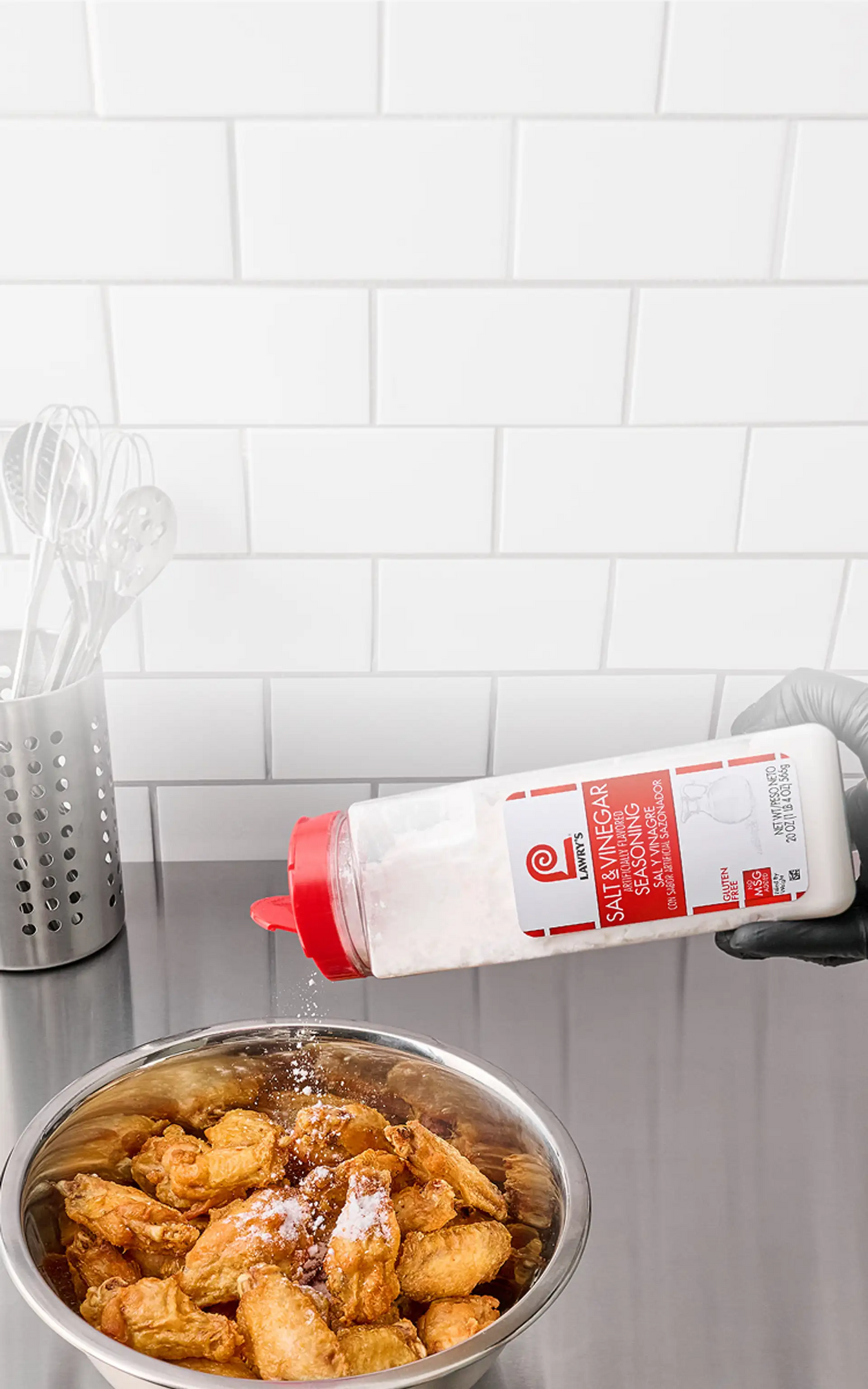 Bowl of fried food with a bottle of seasoning being poured over it on a tiled kitchen counter.