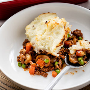 A white plate with a serving of shepherds pie with mashed potatoes on top.