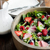 A wooden bowl filled with a salad of fresh greens, strawberries, raspberries, and blueberries, topped with a creamy dressing.