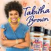 Tabitha Brown, a woman with curly hair, smiles while holding two jars of McCormicks Life Sweet Life Smoky seasoning.