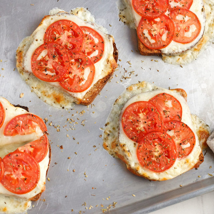 Four slices of toasted bread topped with melted cheese and tomato slices.