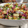 A white bowl filled with potato salad with red onion parsley and bacon.