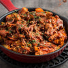 A red cast iron skillet filled with a hearty stew of chicken bacon and vegetables.