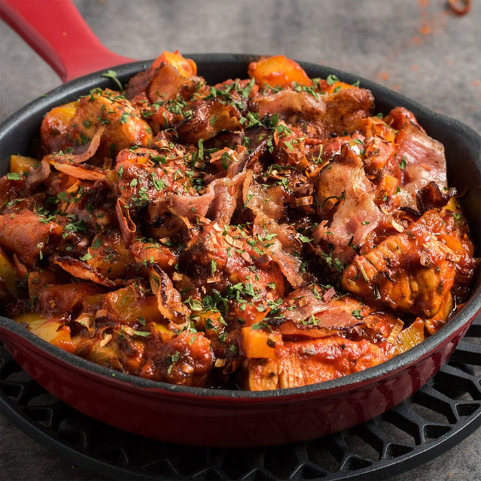 A red cast iron skillet filled with a hearty stew of chicken bacon and vegetables.