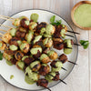 Grilled skewers of beef and potatoes drizzled with a green sauce.