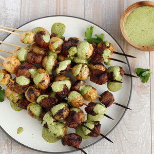 Grilled skewers of beef and potatoes drizzled with a green sauce.