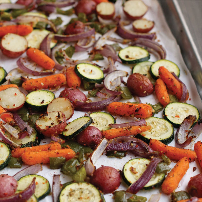 A close-up of a baking sheet with roasted vegetables, including red potatoes, zucchini, carrots, and red onions.