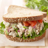 A chicken salad sandwich on whole wheat bread with lettuce tomato and red onion.