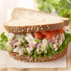 A chicken salad sandwich on whole wheat bread with lettuce tomato and red onion.