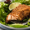 A close-up of a fork with a piece of salmon on top of a bed of lettuce.