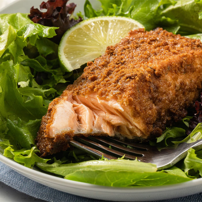 A close-up of a fork with a piece of salmon on top of a bed of lettuce.