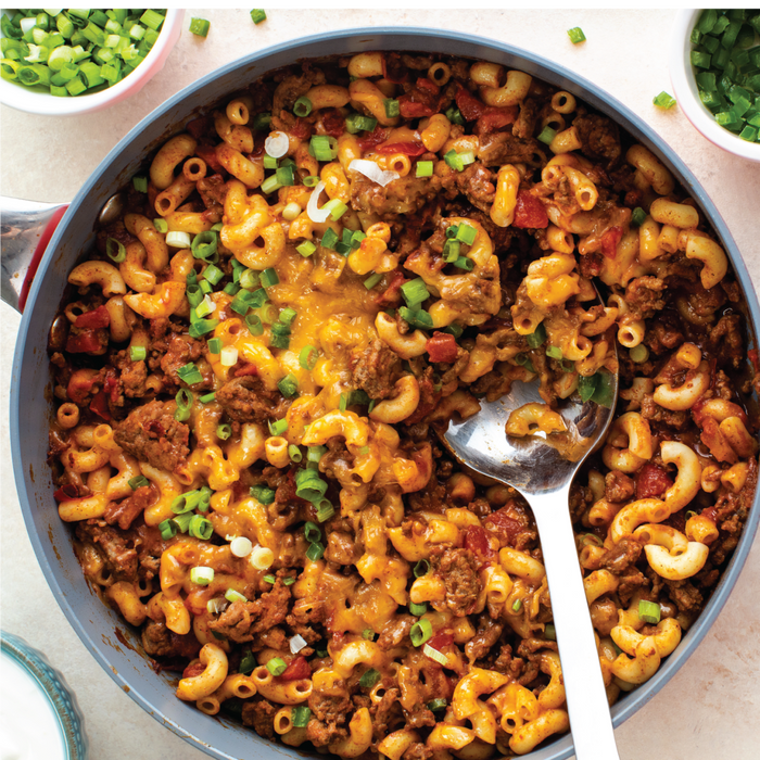 A close-up of a skillet filled with a cheesy ground beef and macaroni dish topped with green onions.