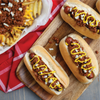 Three hot dogs topped with chili, mustard and onions on a wooden cutting board.