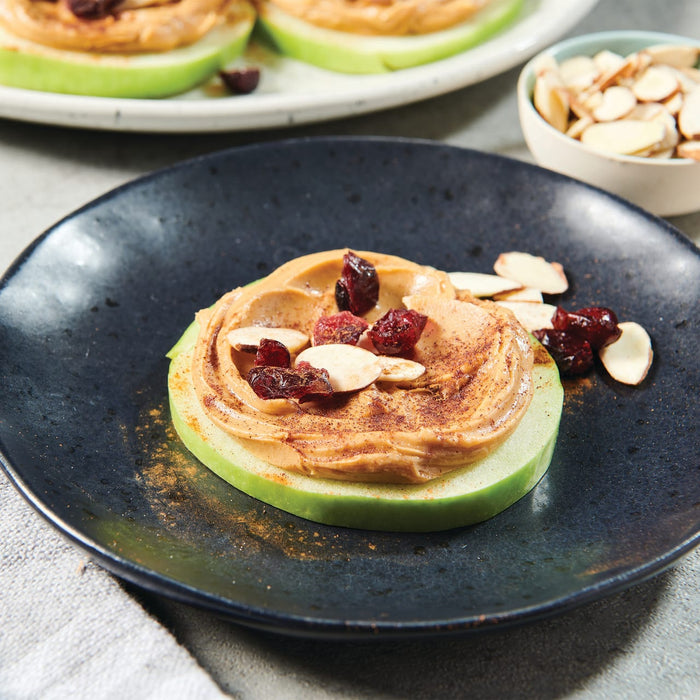 A close-up of a peanut butter and apple snack with cranberries and almonds.