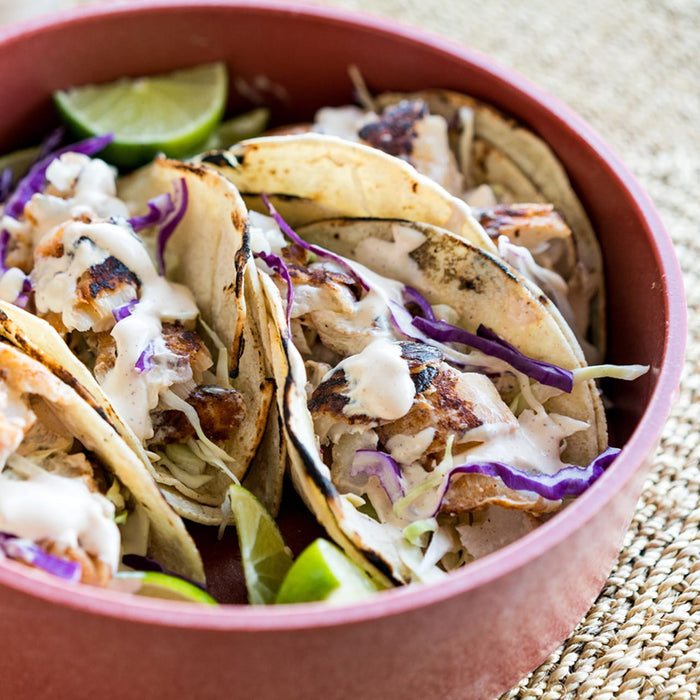 Four tacos filled with fish, cabbage, and a creamy sauce are in a red bowl.