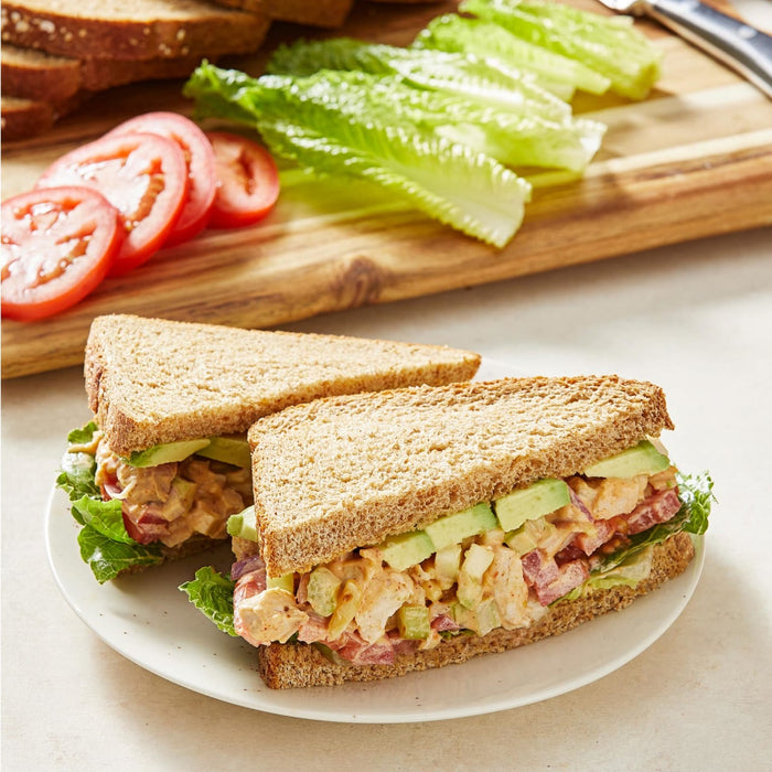 Two chicken salad sandwiches on whole wheat bread with lettuce, tomato, avocado, and celery.