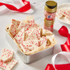 A tin of white chocolate bark with red sprinkles, next to a bottle of McCormick Candy Cane Finishing Sugar.