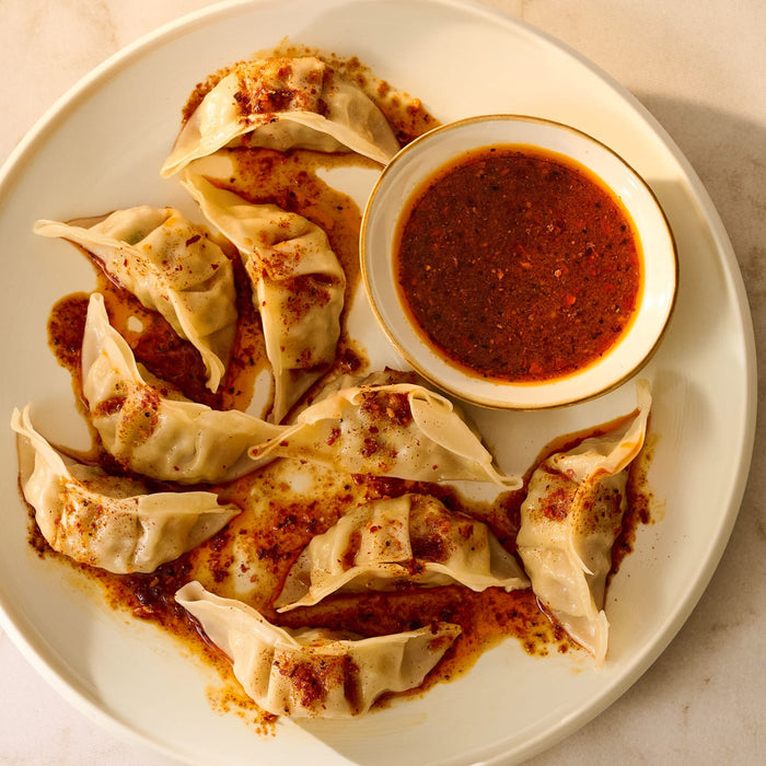 A plate of dumplings is served with a bowl of chili oil sauce.
