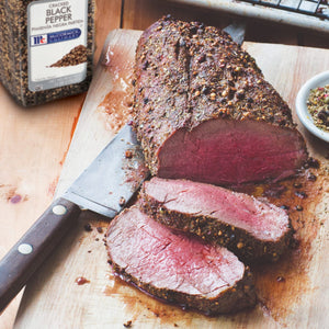 A close-up of a sliced McCormick Culinary Cracked Black Pepper seasoned roast on a wooden cutting board.