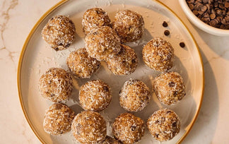 Plate of round brown energy bites on a beige plate with a bowl of chocolate chips in the background.