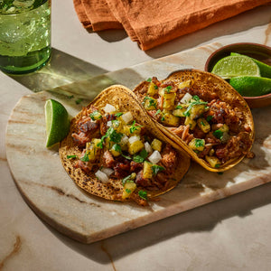 Two appetizing tacos topped with a vibrant salsa and served with lime wedges on a marble board.