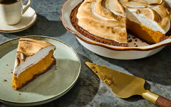 Pumpkin pie with a slice on a plate, pie dish, and serving spatula on a dark surface.