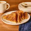 Slices of French toast, generously sprinkled with Mccormick Hufflepuff Finishing Sugar Harry Potter 3.37 Oz, are arranged on a white plate next to a coffee mug and a stack of plates with gold forks.