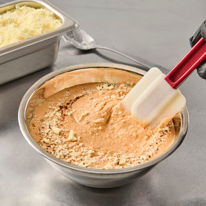 A metal bowl with a creamy sauce and grated cheese being stirred with a red spatula.