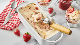Ice cream dish with strawberry swirls, a scoop, and strawberries on a marble surface.