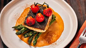 Plated dish with roasted tomatoes, asparagus, and a piece of bread on a white plate.