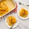 A white baking dish filled with cheesy scalloped potatoes, with two plates of the same dish.