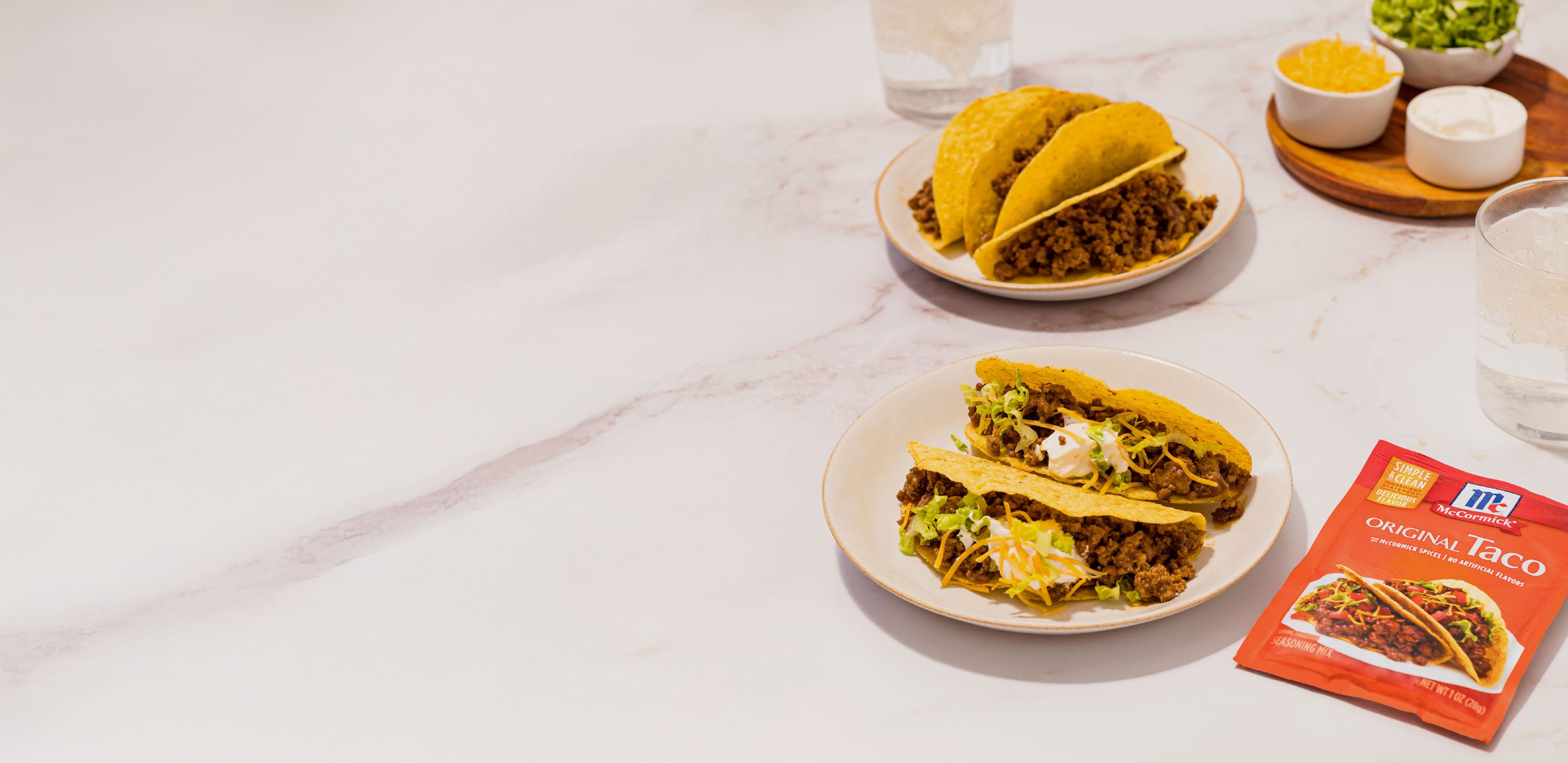 Two plates of tacos on a white table with taco seasoning.