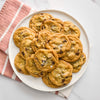 A white plate is filled with golden-brown chocolate chip cookies, generously sprinkled with coarse sea salt, suggesting the use of Mccormick Hss Sea Salt Coarse Ground 13.5 Oz.